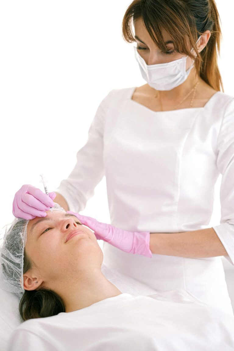 Beautician in mask and gloves preparing an injection for a client during a beauty treatment session.